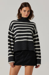 A woman is wearing a black and white horizontally striped turtleneck sweater with a chunky knit design. The sweater features wider black and white stripes and a ribbed hem and cuffs. She pairs the sweater with a black leather mini skirt.